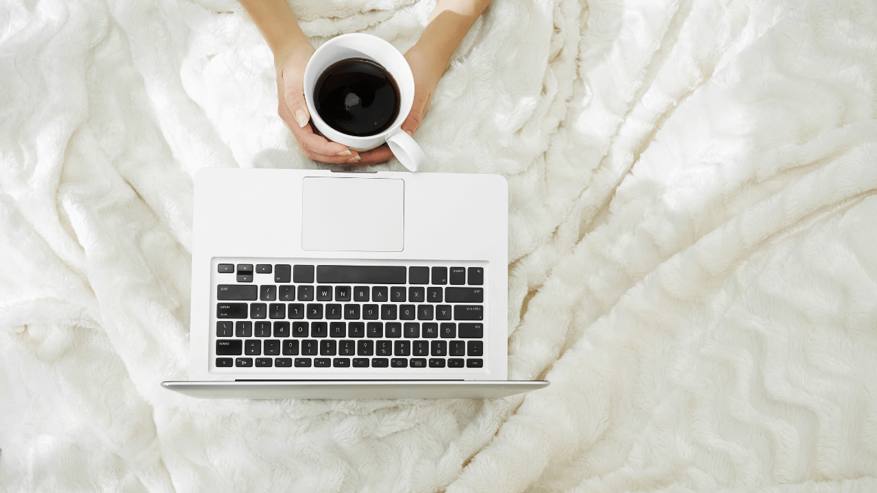 laptop on a blanket with someone holding a cup of coffee
